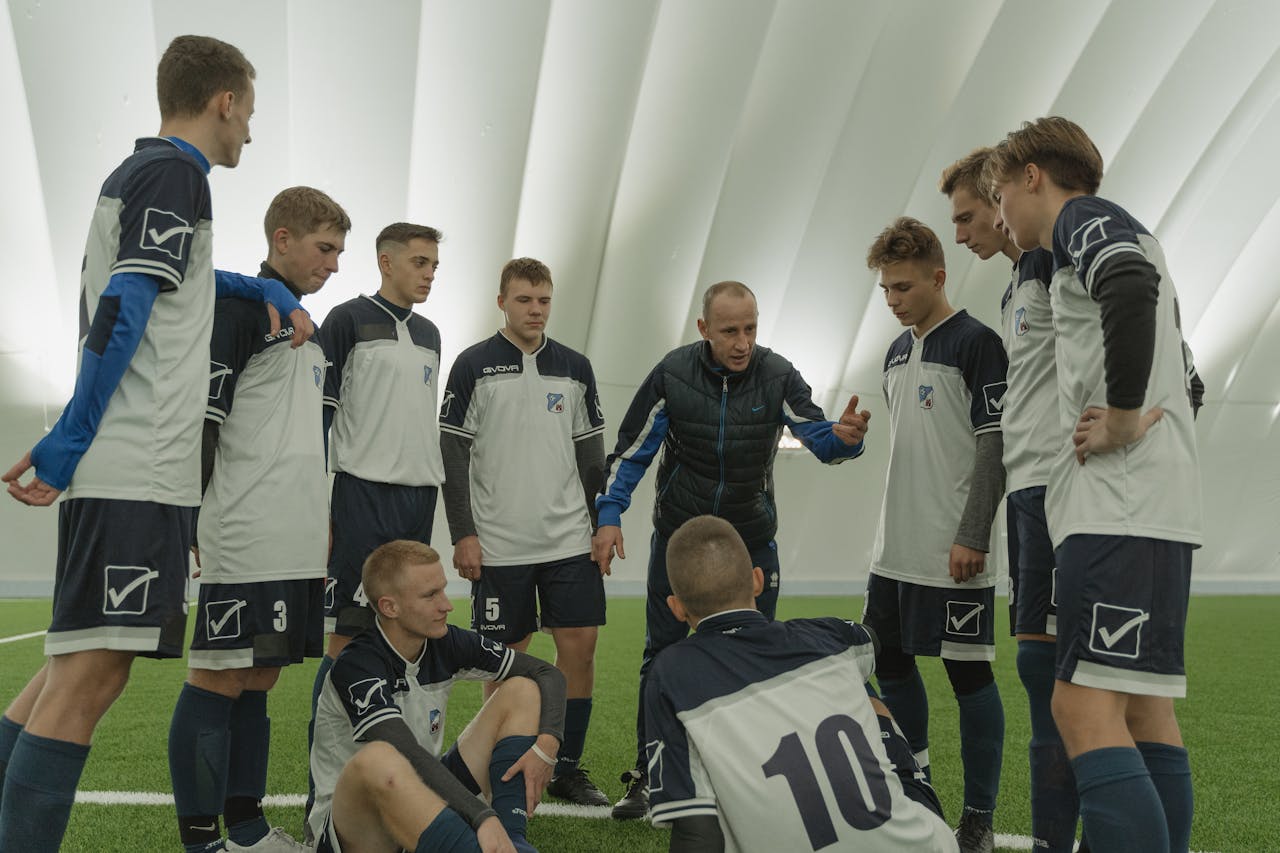 services-04 Coach giving a pep talk to a men's soccer team indoors.