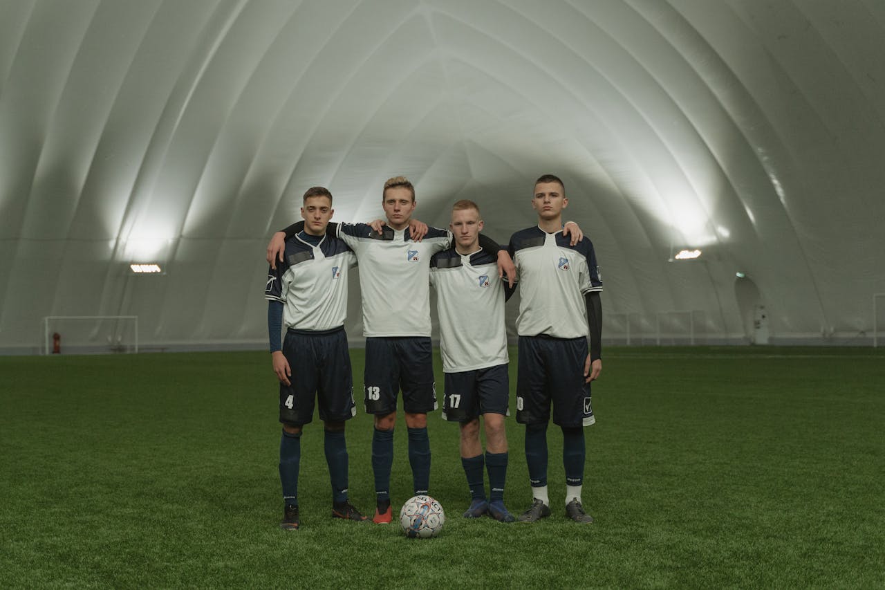 who-we-are Four young soccer players stand together indoors with a soccer ball on artificial turf.